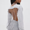 A woman models the OPEN BACK CHAIN DETAIL SWEATSHIRT IN GREY, featuring silver chain accents. Captured from the side against a plain background, she completes her street style with large hoop earrings and sleek hair over one shoulder.