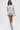 A woman wearing the OPEN BACK CHAIN DETAIL SWEATSHIRT IN GREY, matching shorts, layered silver necklaces, and slouchy gray boots walks confidently against a plain white background, showcasing effortless street style.