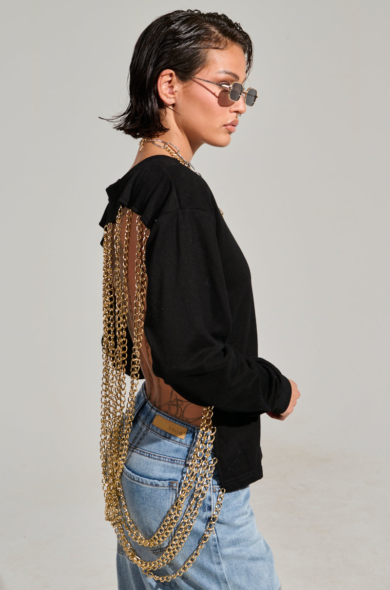 A person with short hair sports a casual look, wearing sunglasses and an OPEN BACK CHAIN DETAIL SWEATSHIRT in black, paired with light blue jeans. They stand against a plain background, looking to the side.