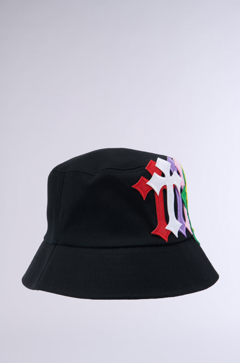 The CROSSED PATCH BUCKET HAT, made from a cotton base, is displayed against a plain background. This hat features colorful embroidered designs with intricate and overlapping T-shaped symbols in red, white, purple, and green. 2