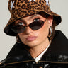 A person wearing the WEAR MY STARS CHEETAH BUCKET HAT, oval-shaped dark sunglasses, hoop earrings, and a black leather jacket gazes directly at the camera against a neutral background.