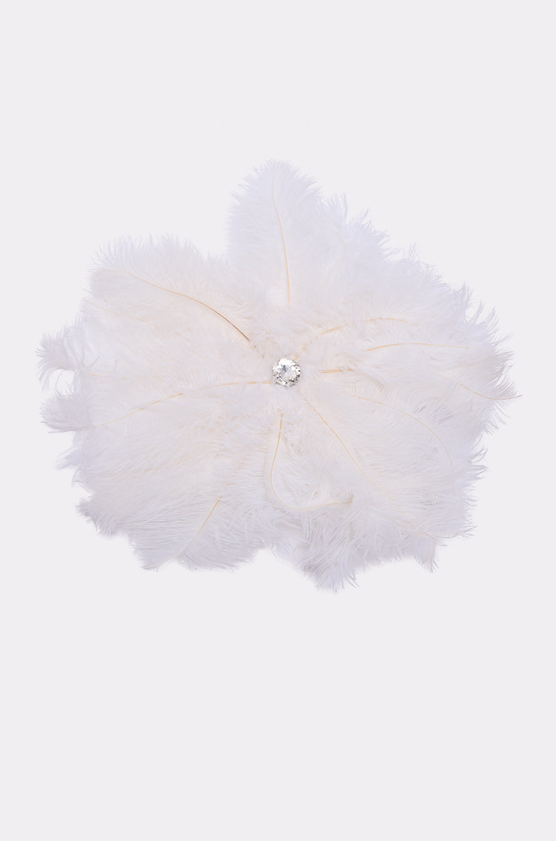 The TREAT YOURSELF FEATHER BROOCH is a white ostrich feather brooch with a floral design and a round sparkling gemstone center, shown against a plain light background. 2
