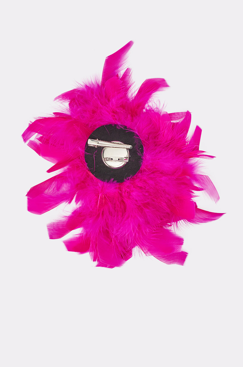 The AT BRUNCH FEATHER BROOCH features bright fuchsia feathers in a circular design with a silver pin backing, displayed on a plain white background—a bold statement piece for any outfit. 5