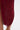 Close-up of the SOFIA FRINGE HIGH SLIT MIDI DRESS IN BURGUNDY, featuring long fringe layers, a high slit revealing a leg and gold sandal, set against a plain white background.
