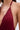 Close-up of a person wearing the SOFIA FRINGE HIGH SLIT MIDI DRESS IN BURGUNDY, featuring deep red pleated fabric with thin straps and gold accents, highlighting the upper chest, shoulder, and part of the side.
