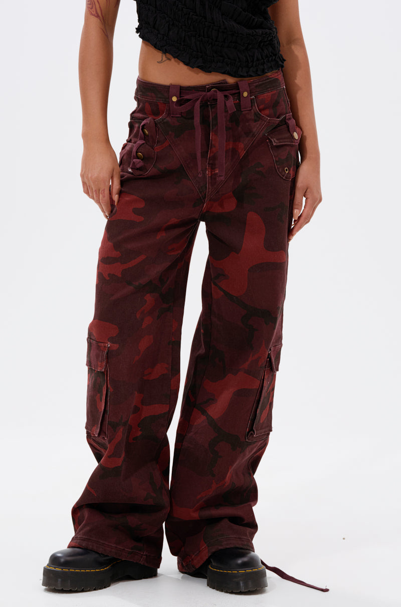 A person wears the CANT SEE ME BURGUNDY CAMP CARGO JOGGER with a black cropped top and black platform shoes, standing against a plain white background. 0