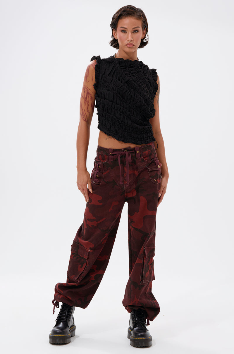 A woman with short dark hair and arm tattoos exudes bold streetwear style in a sleeveless black ruffled top, CANT SEE ME BURGUNDY CAMP CARGO JOGGER pants, and black combat boots against a plain white background. 6