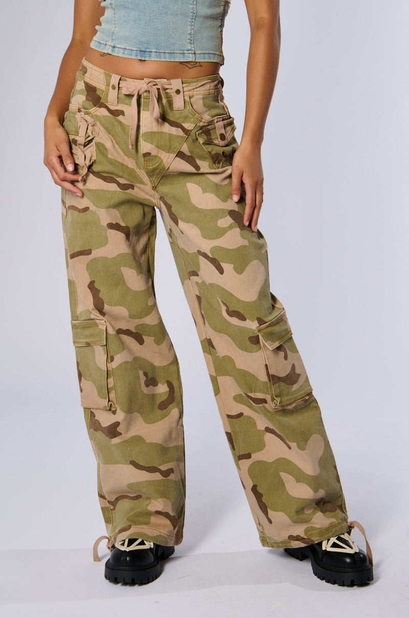 A person is wearing a light blue crop top and the ON TOP OF IT CAMO JOGGER with multiple cargo flap pockets and drawstring details. With their hands in the pockets near their hips, they also sport black chunky-soled lace-up shoes.