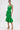A woman poses in the LET'S GO TO THE BEACH RUFFLE MIDI DRESS IN GREEN, a sleeveless fitted summer dress with eyelet lace and a flared ruffle hem. She completes the look with hoop earrings and platform sandals against a white background.