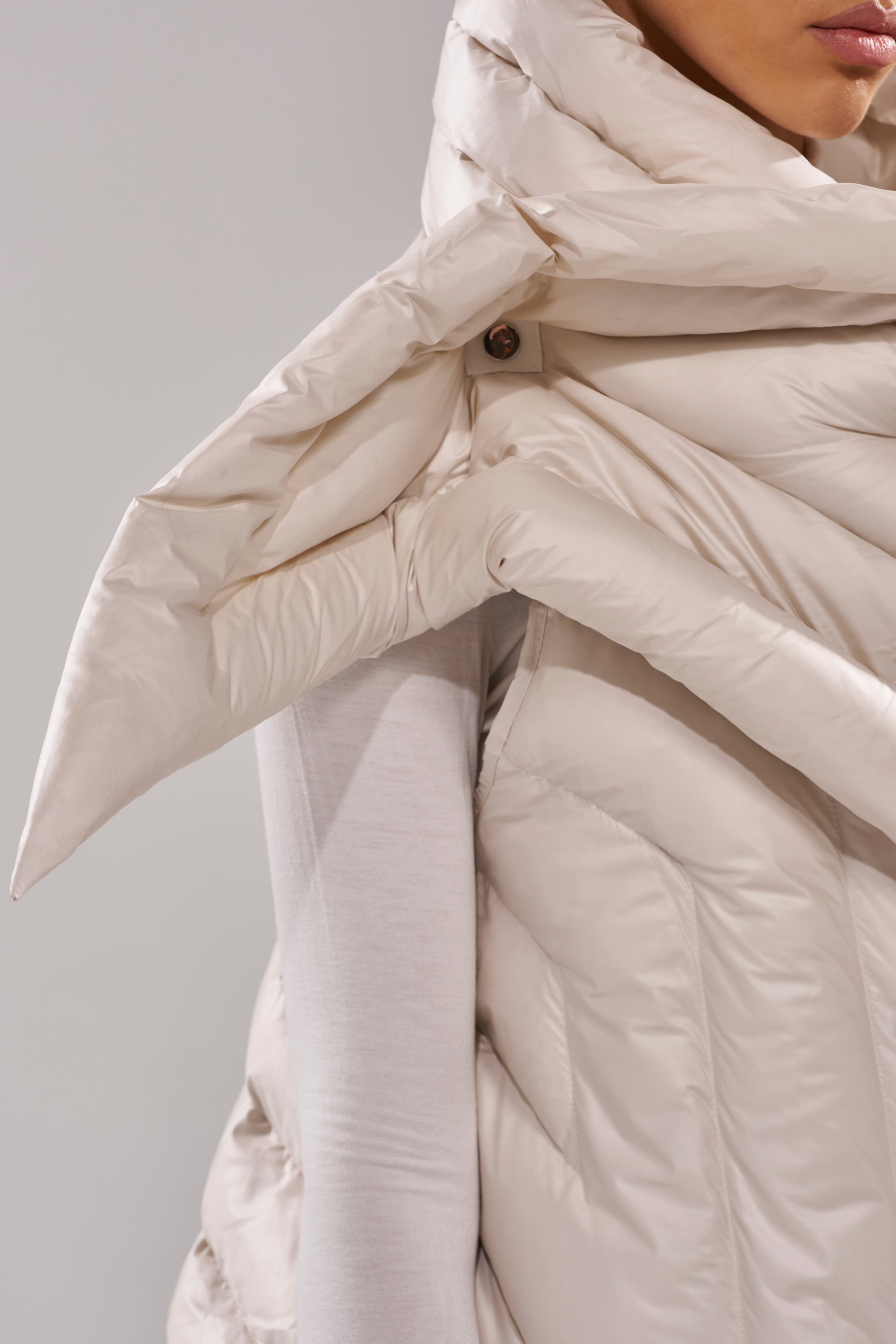Close-up of a person wearing the FOR THE DRAMA PUFFER VEST IN IVORY, featuring an oversized collar, pointed shoulder detail, and wrap-around design over a light long-sleeve top. 4