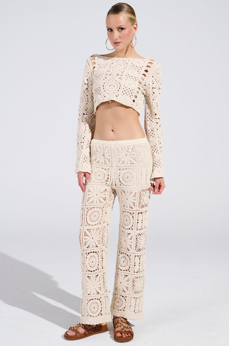 A person poses confidently in the CROCHET KNIT CROP TOP set, exuding a sun-kissed vibe. Paired with large hoop earrings and brown sandals, the look creates a beachy dream against a plain white background.