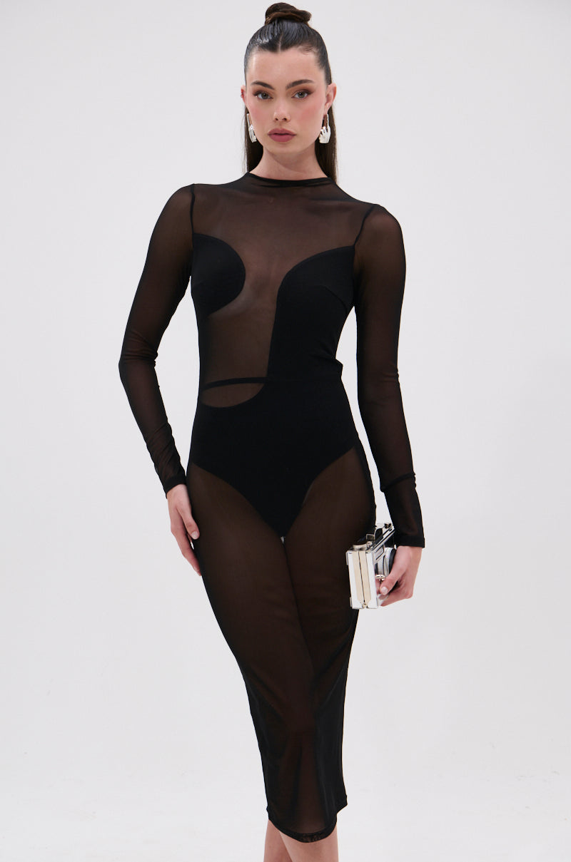 Woman wearing the MINDING MY BUSINESS MESH MIDI DRESS—sheer black mesh, long sleeves, geometric panels—holds a small purse against a plain white background.