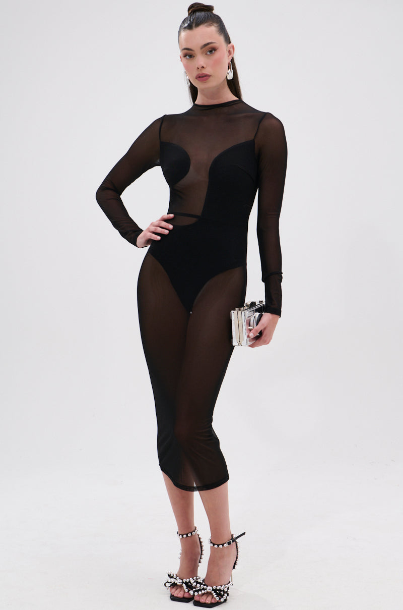 A woman poses against a plain background wearing the MINDING MY BUSINESS MESH MIDI DRESS over a black bodysuit, holding a small clutch, with her hair in a high ponytail and pearl-adorned heeled sandals.