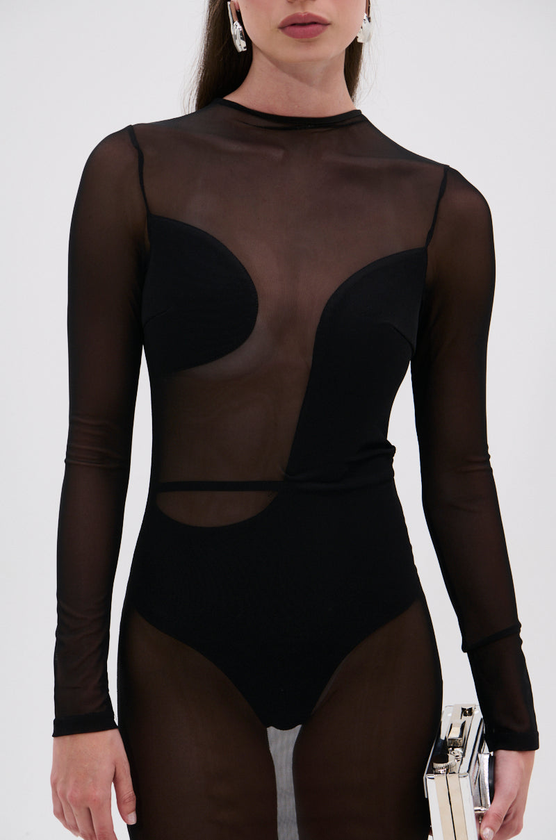A woman wears the MINDING MY BUSINESS MESH MIDI DRESS, featuring sheer mesh with bold black designs over a bodysuit, and holds a small rectangular clutch against a plain light background.