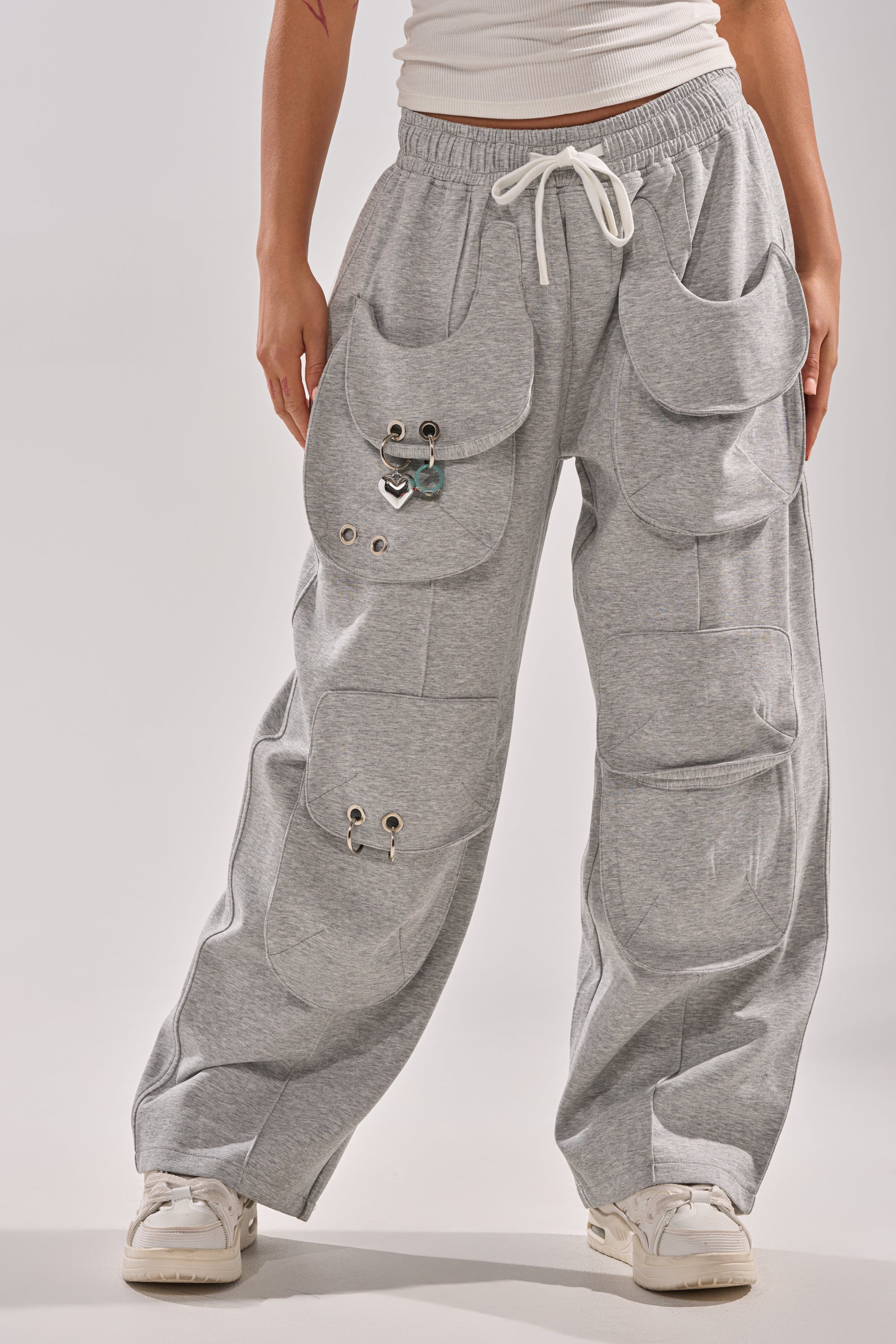 A person styles the GET WITH IT WIDE LEG CARGO JOGGER in gray—featuring layered pockets, metal grommets, carabiner clip, and a white drawstring—with white sneakers and a white top for a fresh streetwear vibe. 1