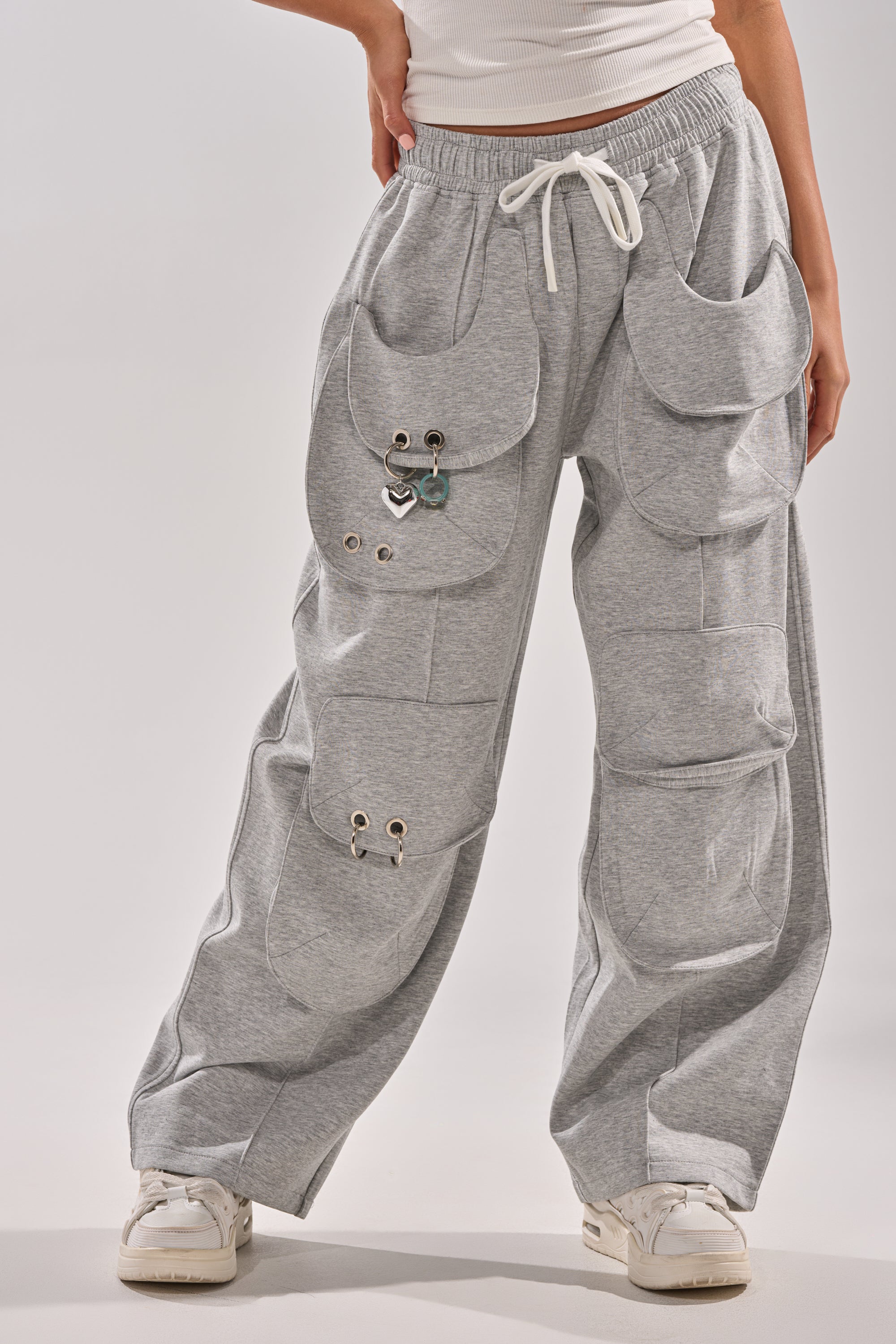 Wearing the GET WITH IT WIDE LEG CARGO JOGGER in grey—loose fit with large pockets, metal grommets, and rings—styled with white sneakers and a ribbed white top. Photo is cropped above the waist. 2