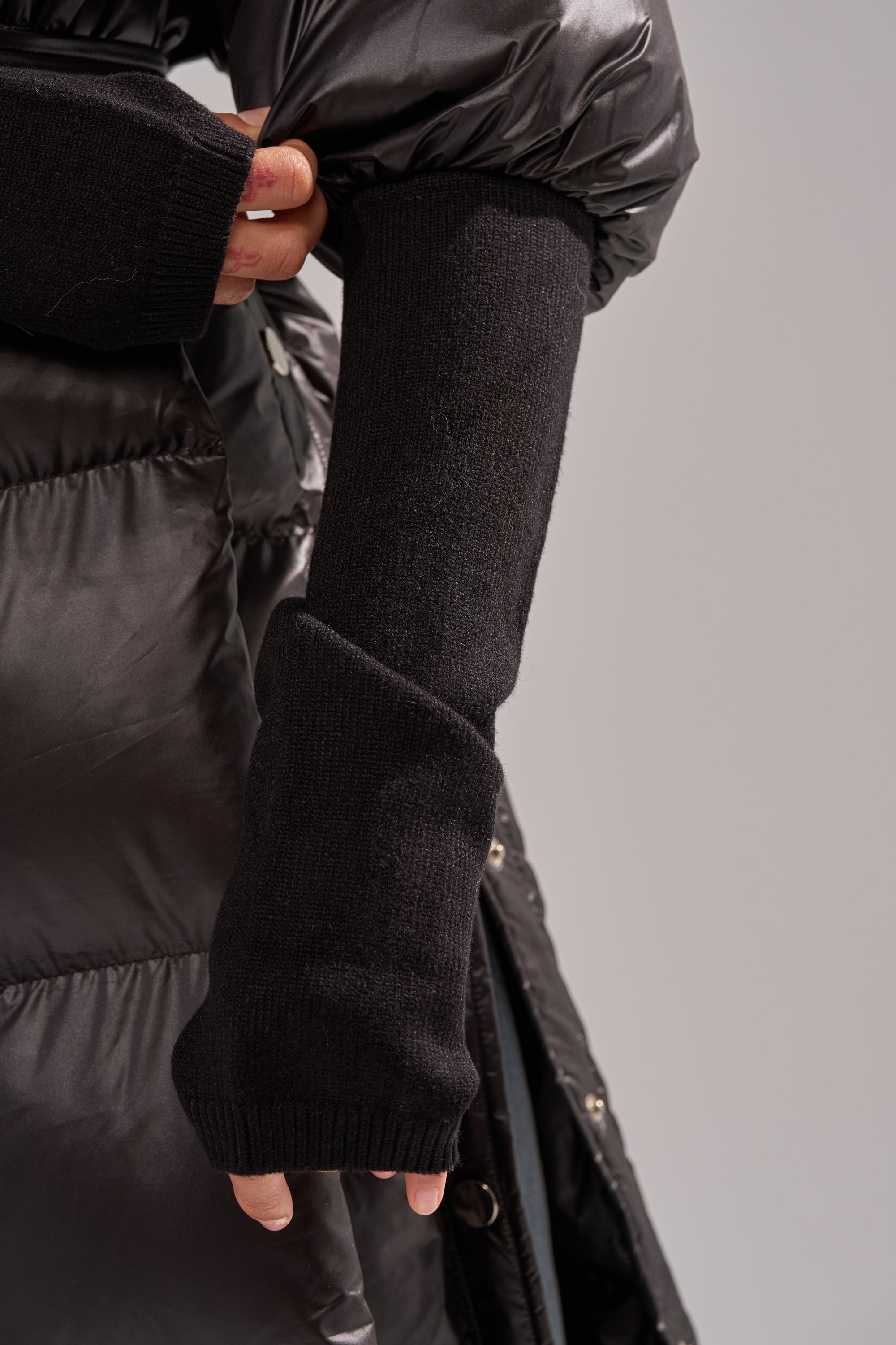 Dressed in the POPPIN OFF TEARAWAY PUFFER and long black knit fingerless gloves, a person raises one arm while adjusting their sleeve.
