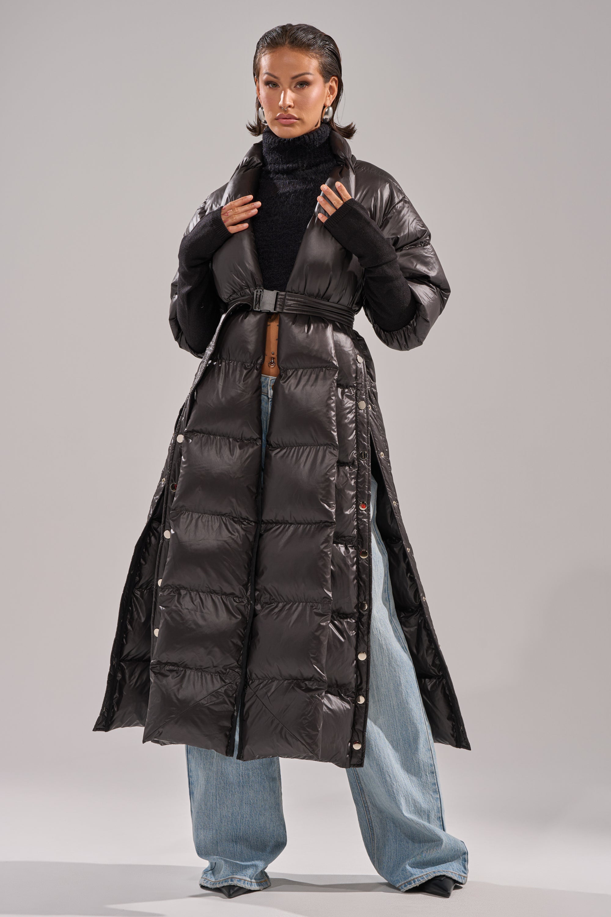 A woman poses confidently in the POPPIN OFF TEARAWAY PUFFER, styled with a black turtleneck sweater and wide-leg blue jeans against a plain light gray background.