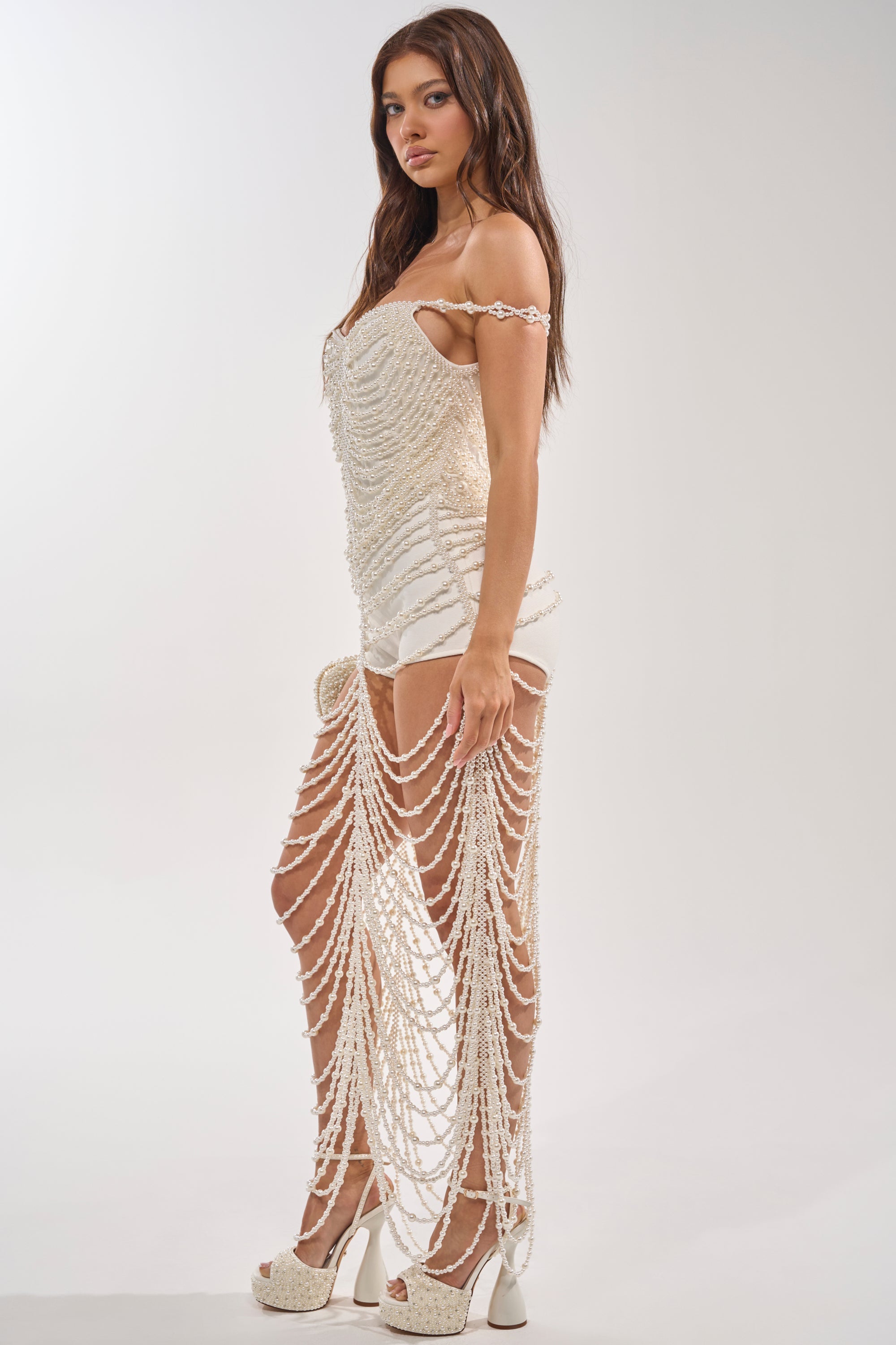A woman in profile models the "DRESSED UP FOR THE BEST PEARL MAXI DRESS," featuring pearl embellishments and draped chains, paired with high-heeled sandals—an elegant choice for bridal celebrations or formal events against a light backdrop. 3
