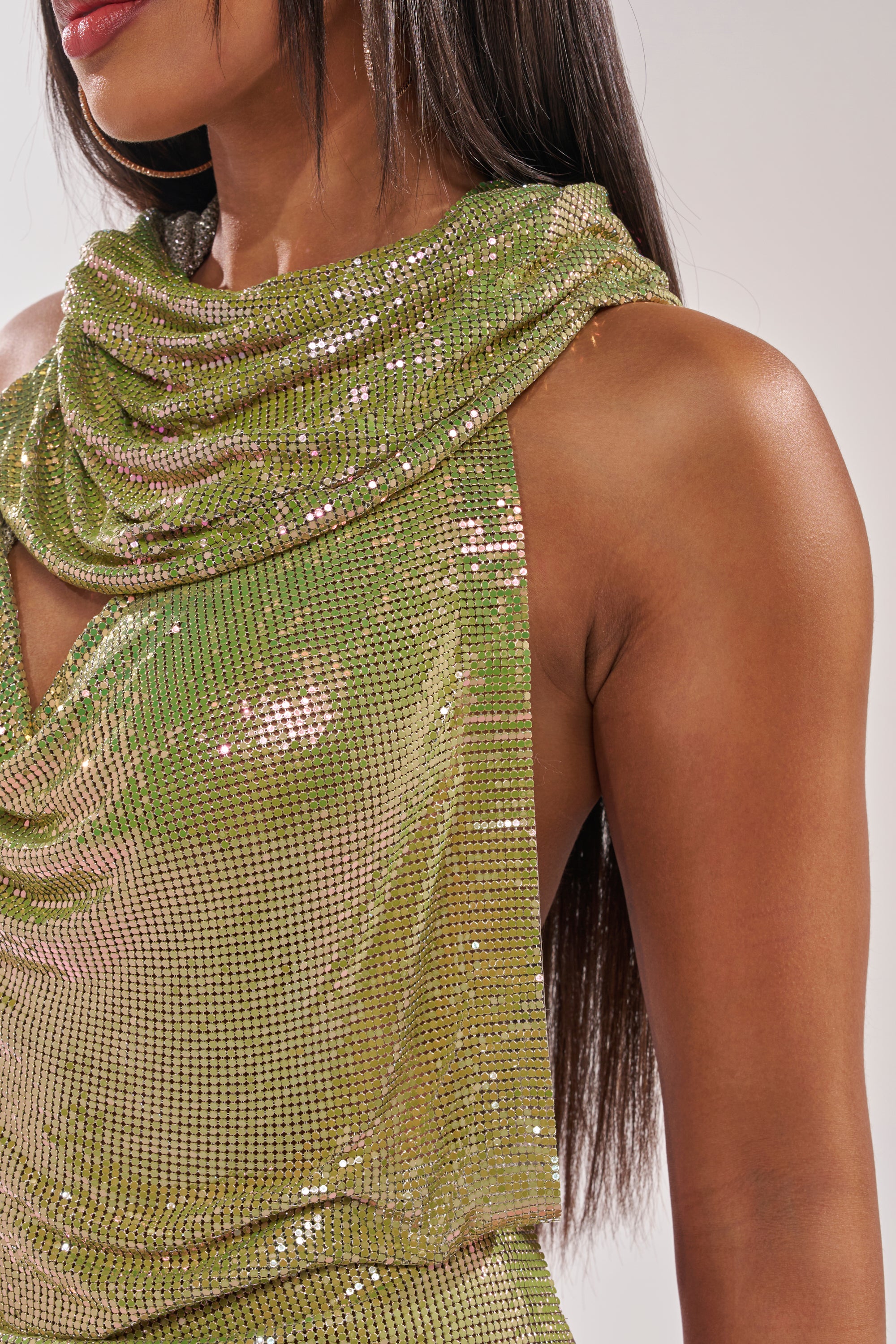 A woman with long straight hair wears the IN MY MIND HOODED CHAINMAIL TOP IN GREEN, featuring a shiny sequined finish and draped neckline. Her face is partially visible, highlighting the shimmering fabric. 8