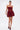 A woman in the BELINA Lace Mini Dress with Bubble Skirt in Burgundy, featuring a strapless lace design and voluminous skirt, stands against a white background with a clutch and matching platform heels.