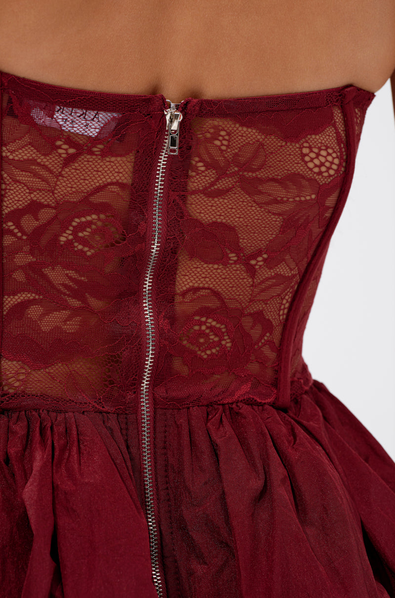 Close-up of the BELINA LACE MINI DRESS WITH BUBBLE SKIRT IN BURGUNDY, showing sheer floral lace at the back, a visible silver zipper, and a gathered burgundy bubble skirt silhouette.
