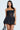 Wearing the BELINA LACE MINI DRESS WITH BUBBLE SKIRT, a woman showcases a strapless black outfit featuring a fitted lace bodice and bubble skirt. Her long hair flows elegantly with hoop earrings, accessorized by a sleek black bag, all set against a light gray background.