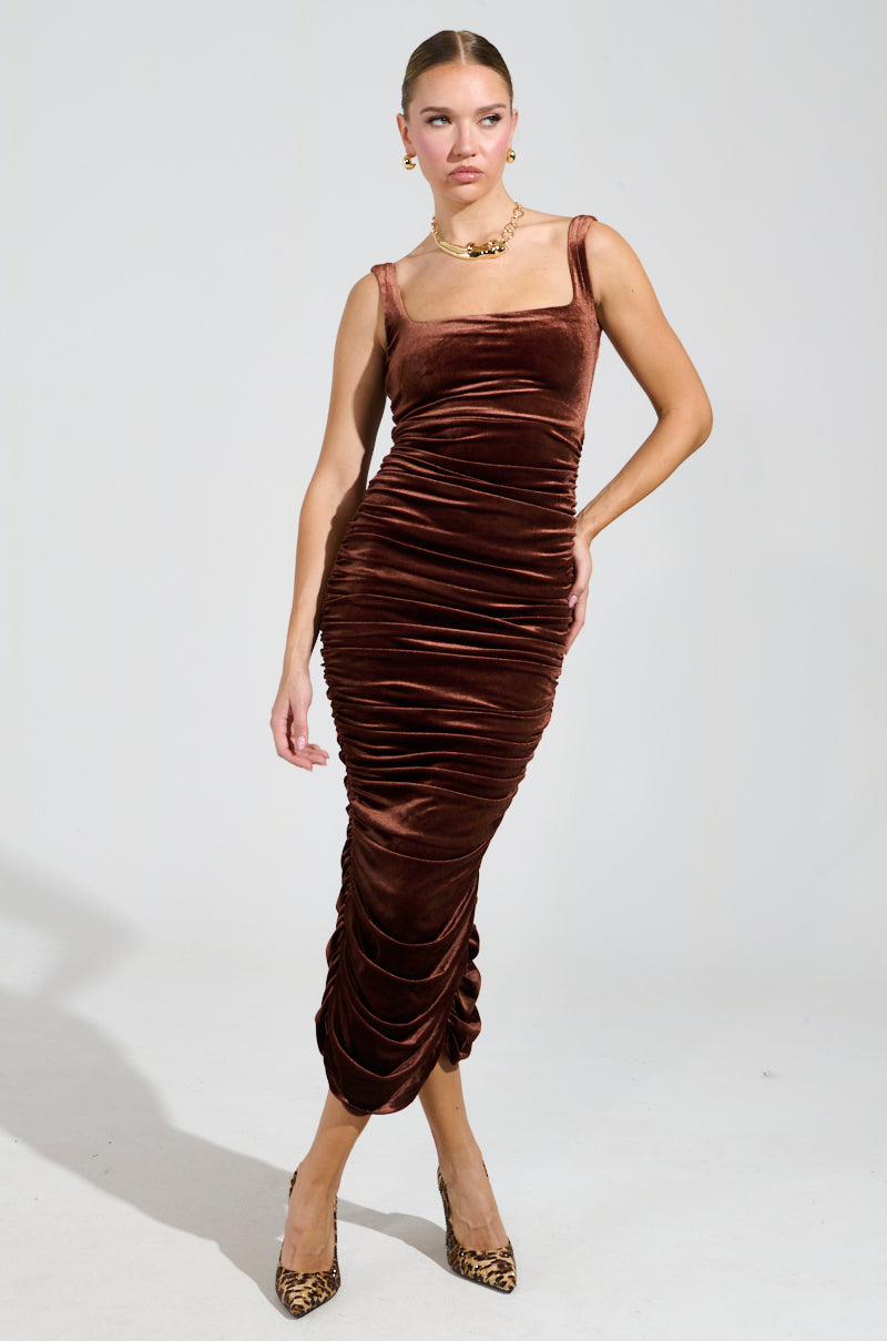 Dressed in the FOR EVERYONE VELVET MIDI DRESS, a person exudes confidence with its brown, ruched design. They complete the look with leopard-print heels, hoop earrings, and a chunky gold necklace against a simple, light-colored background.