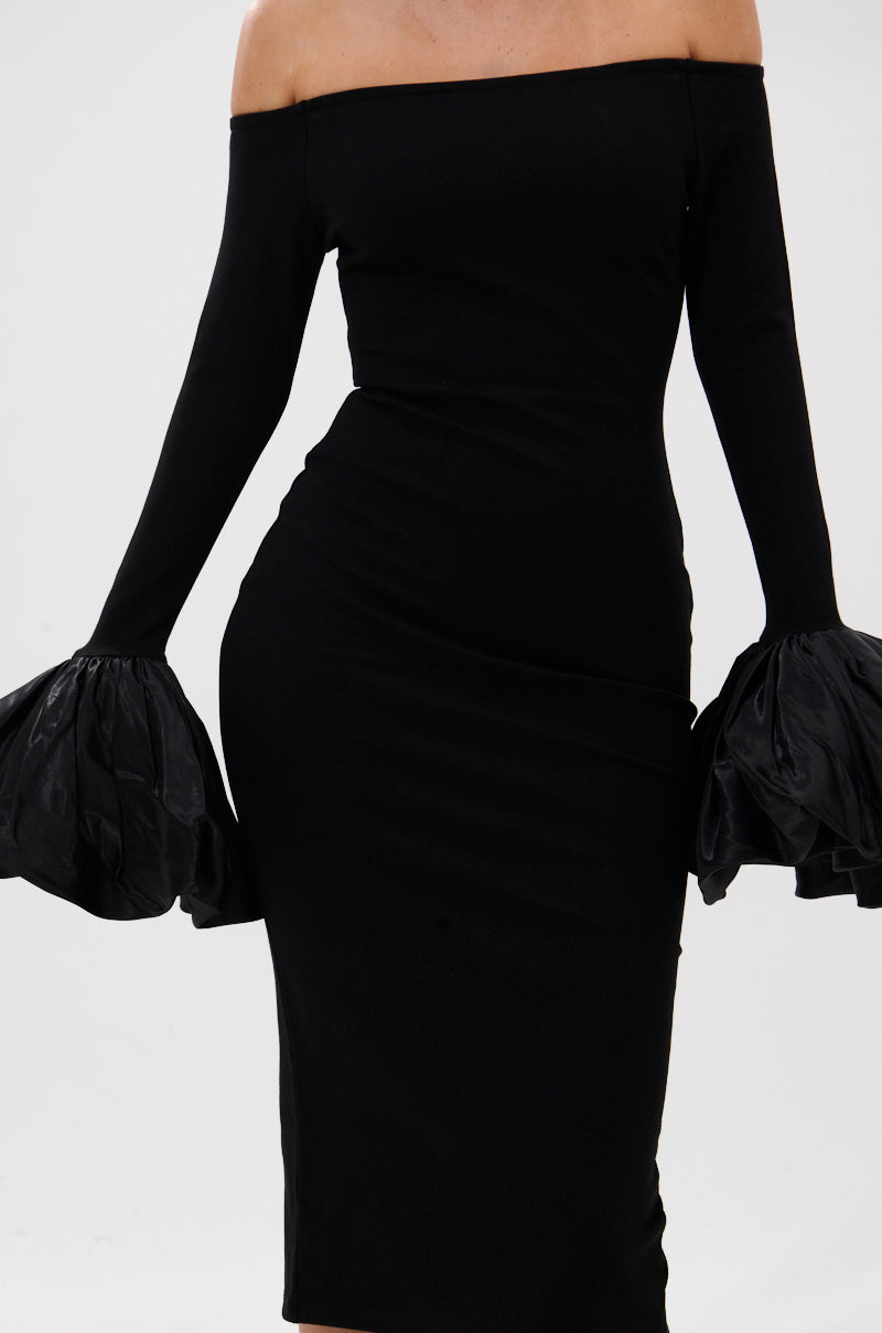 A model showcases the "CLASS WITH A LITTLE BIT OF SASS MIDI DRESS," a form-fitting, black, off-the-shoulder cocktail dress with long sleeves and bold ruffled cuffs; the image focuses on the torso without showing face or legs.