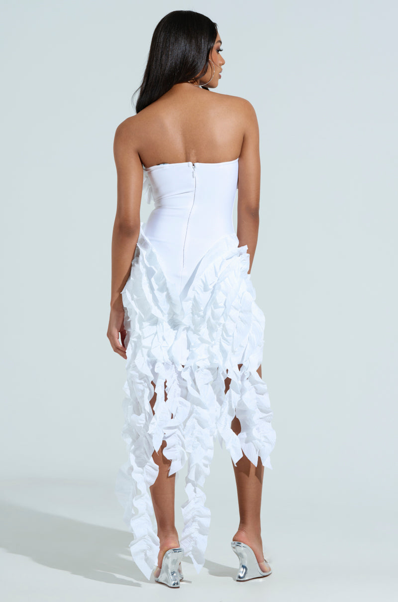 Against a light background, a woman with flowing dark hair wears the City Lights Ruffle Midi Dress in white. The cascading ruffled tendrils of her strapless gown complement her silver high heels, and the dress elegantly finishes with a zipper at the back.