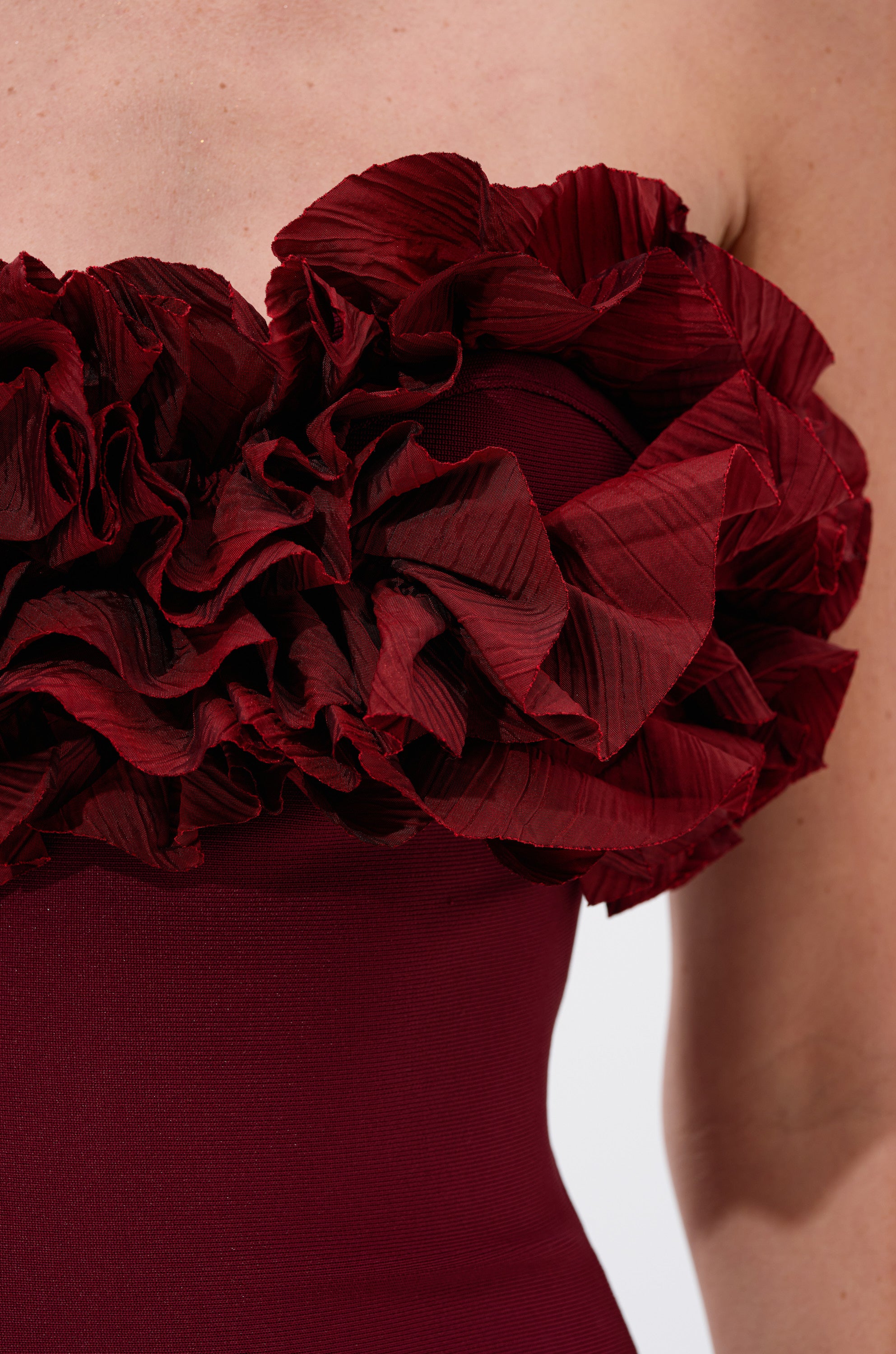 Close-up of a person wearing the CITY LIGHTS RUFFLE MIDI DRESS IN BURGUNDY, featuring a strapless design with textured ruffled layers and pleats along the top edge for an elegant, eye-catching look.