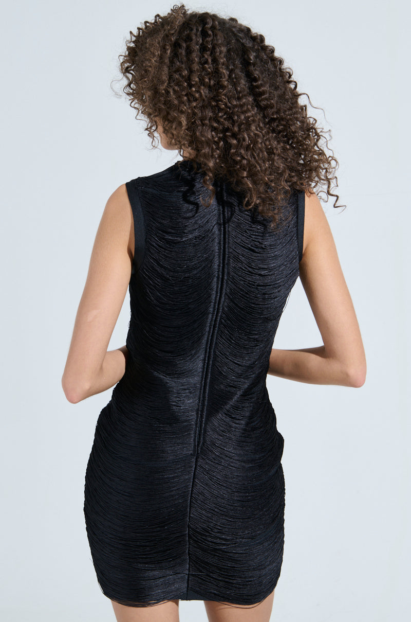 A person with curly hair wears the SHE'S SOPHISTICATED BANDAGE MINI DRESS, a black sleeveless dress with a bodycon fit and notable zipper detail. They face away, set against a plain light gray backdrop that highlights the elegance of the LBD.