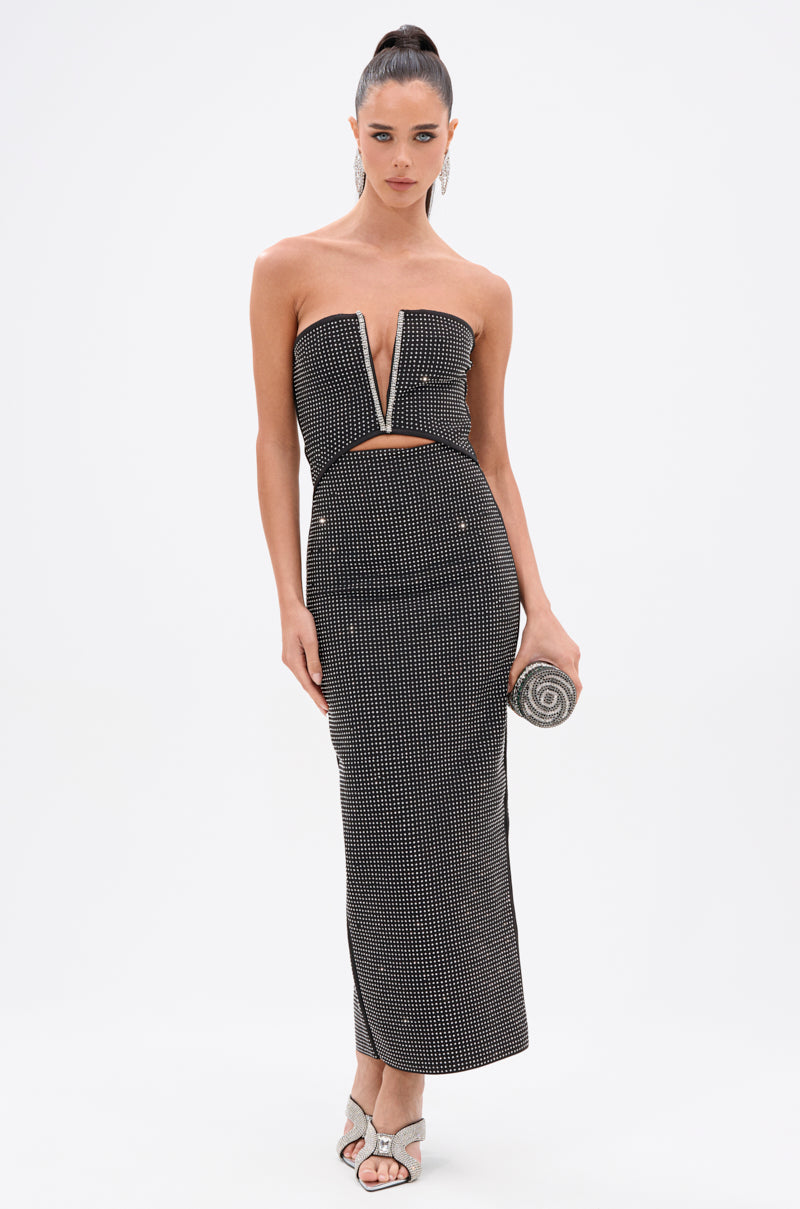 A woman in the ALINA RHINESTONE MIDI DRESS—a strapless, black-and-white bodycon style with a deep V and waist cutout—holds a silver clutch and wears white heeled sandals against a plain white background.