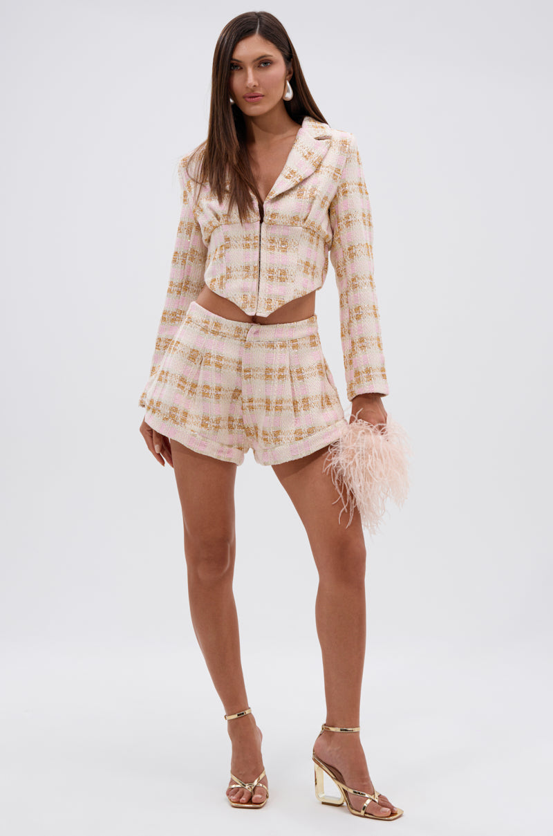 A woman exudes confidence in the FLORENCE TWEED BLAZER with matching high-waisted shorts, pairing them with a blush pink feathered clutch and gold open-toe heels. Her long straight hair frames her neutral expression. 4