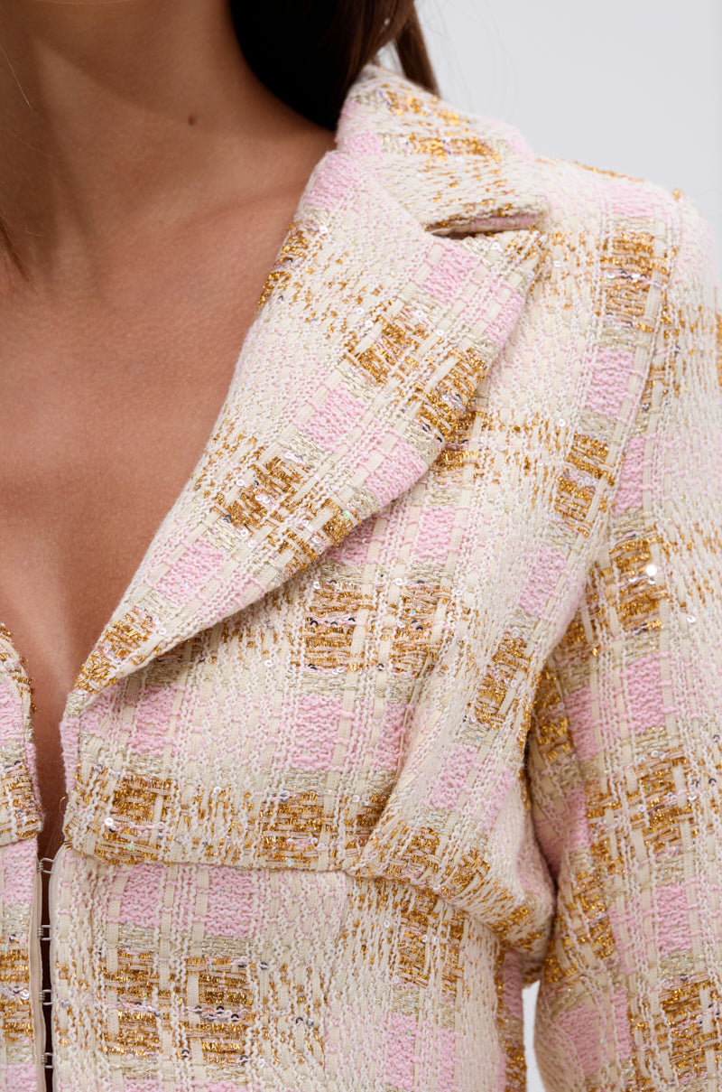 Close-up of a woman wearing the FLORENCE TWEED BLAZER, a cropped pastel pink jacket in cream, pink, and gold with metallic threading, notched collar, and part of her neck and chest visible. 7