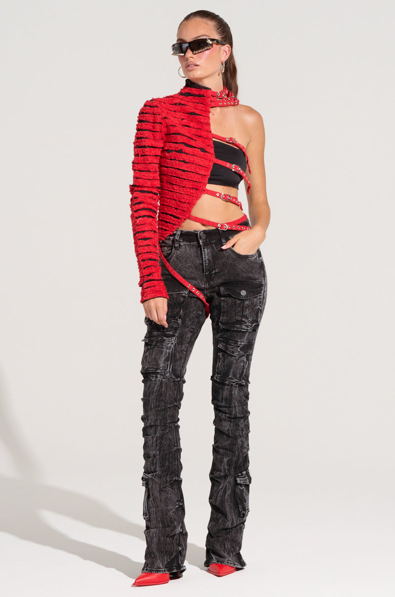A person styled in a fashionable ensemble featuring the PRETTY RECKLESS DISTRESSED DENIM HALF THERE TOP in red, paired with a black bandeau and textured black pants in a chic color block style. They complete the look with sunglasses and red pointed shoes, standing against a neutral background.
