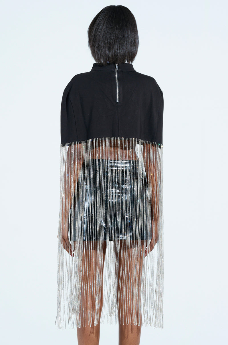 Facing away, a person exudes ultra-glam with the NEW LEVEL SHINE CROPPED BLOUSE, a black top featuring a high collar and silver rhinestone fringe. Paired with a shiny black skirt, long fringes cascade below the knees on a plain background.