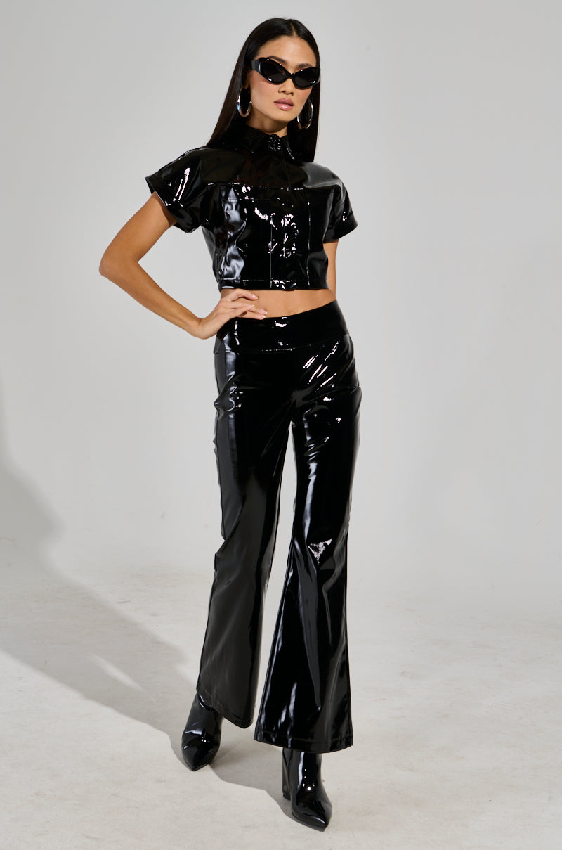 Wearing the SEXY FOX BUTTON DOWN TOP IN BLACK and paired with flared pants, this confident individual exudes style. Their long hair flows effortlessly as they accessorize with black sunglasses and hoop earrings. Striking a pose against a plain background, they embody the essence of AKIRA Label's bold fashion statement.