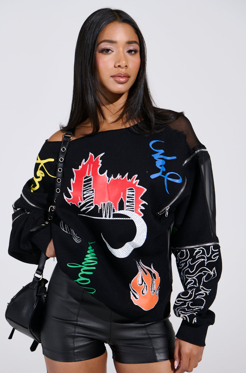 A woman wears the DEEP THOUGHTS OVERSIZED GRAPHIC SWEATSHIRT featuring colorful designs, paired with black leather shorts. Her long, straight hair complements a chic black handbag against a plain light backdrop, emphasizing her modern style.