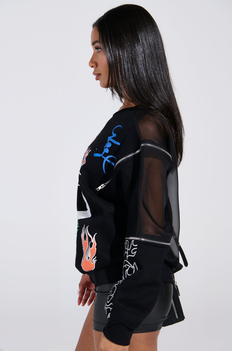 A woman with long, straight hair wears the "Deep Thoughts" oversized graphic sweatshirt featuring colorful designs and sheer mesh accents. Standing in profile against a light gray background, she effortlessly highlights the cotton-blend fabric's casual elegance.