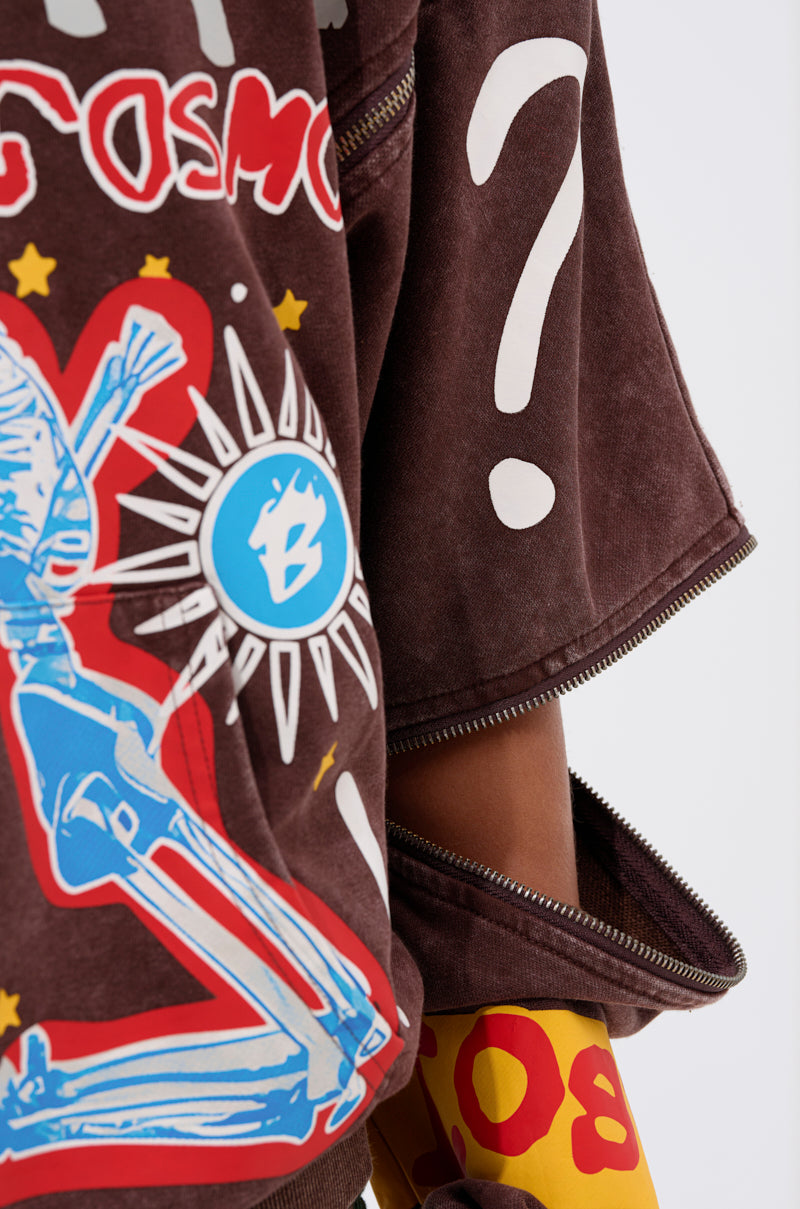 A close-up shows someone wearing the INFINITE COSMOS OVERSIZED GRAPHIC SWEATSHIRT, featuring bold graphics—a large white question mark, blue skeletal figure, yellow and red accents, and zippers—that add flair to the brown piece.