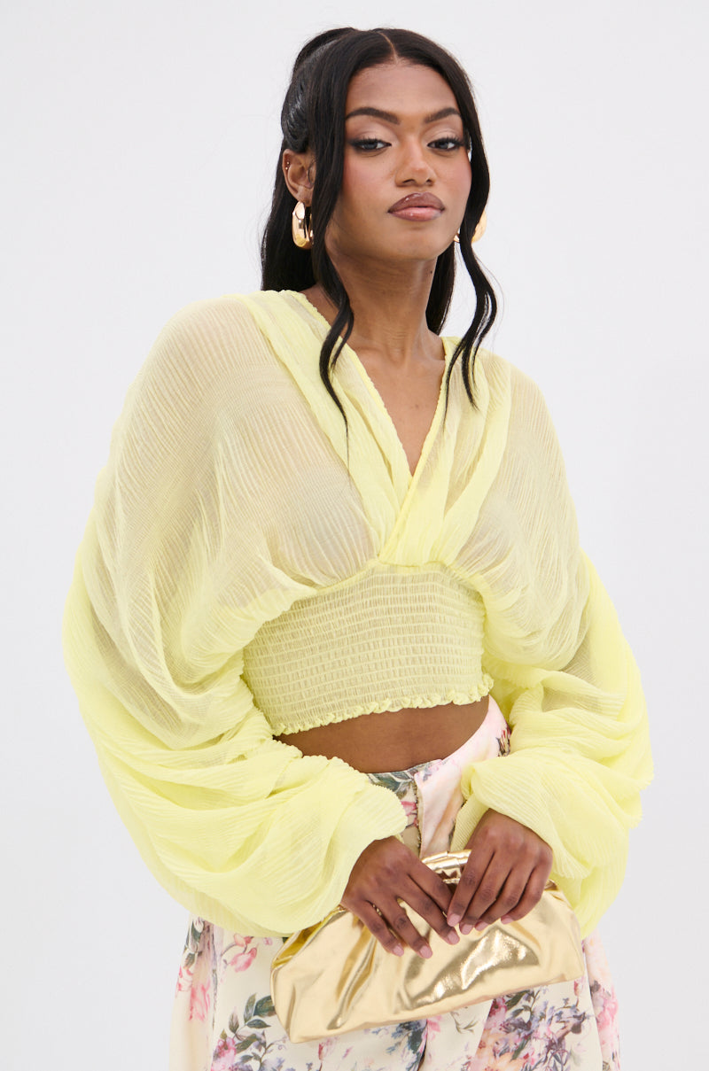 A person with long hair wears the "DIVINE RIGHT LONG SLEEVE BLOUSE TOP" in lemon yellow with sheer puff sleeves and patterned pants, holding a gold clutch bag against a plain white background.