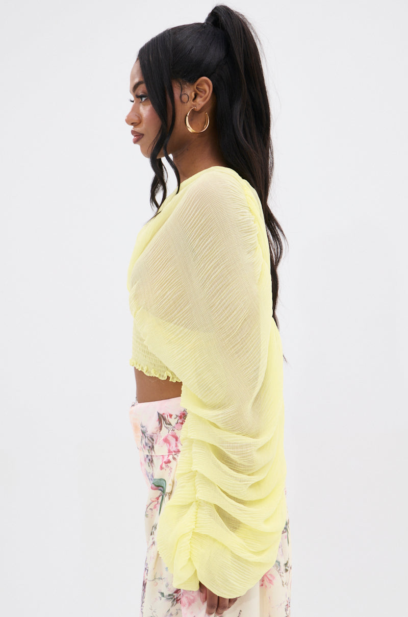 A woman with long black hair in a high ponytail wears the DIVINE RIGHT LONG SLEEVE BLOUSE TOP in lemon yellow chiffon, paired with a floral skirt. Gold hoop earrings complete her look as she gazes forward against a white studio backdrop.