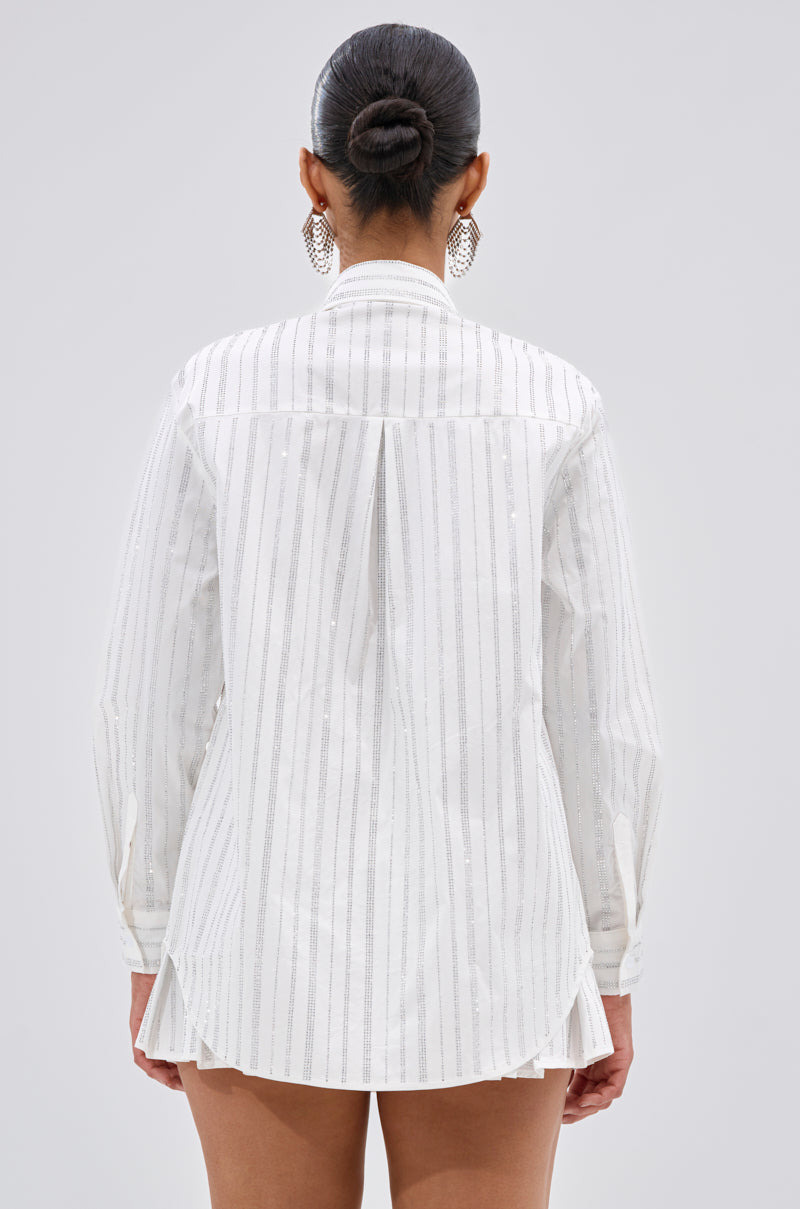 A person with their hair in a bun, wearing large hoop earrings and the ONTO THE NEXT EMBELLISHED BUTTON DOWN TOP IN WHITE, is shown from the back against a plain background. 3
