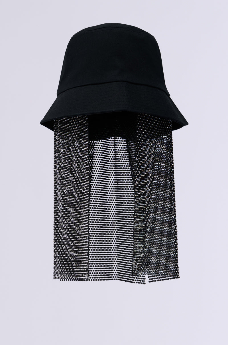 The STRAIGHT DRIPPIN BUCKET HAT IN BLACK boasts a chic design with a fishnet mesh veil that gracefully drapes from the brim, elegantly covering the face area. Enhanced by rhinestone detailing, this stylish accessory is tastefully suspended against a light gray background, making a bold fashion statement.