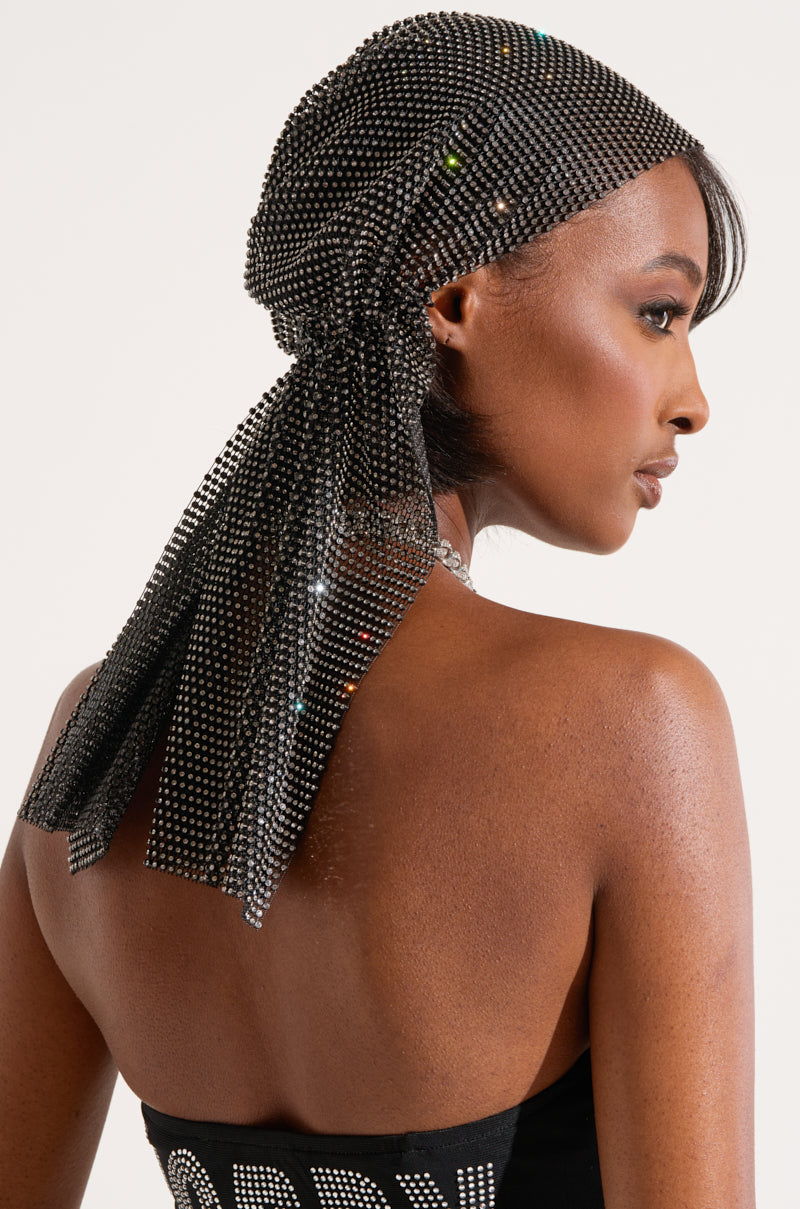 A woman with dark skin is adorned with the ELEGANCE IS EARNED HEADPIECE, a shiny rhinestone mesh that drapes elegantly down her back. She faces sideways, showcasing her bare shoulders and the back of her head. Complementing the headpiece, she wears a black, strapless top. 3