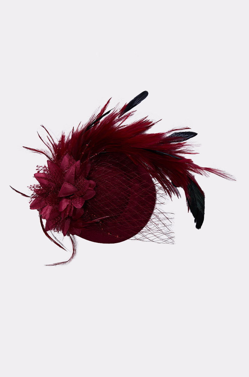 The TOP OF THE DAY CLIP ON FASCINATOR in red features large feather plumes, mesh netting, and layered fabric flowers, displayed against a plain light gray background. 5
