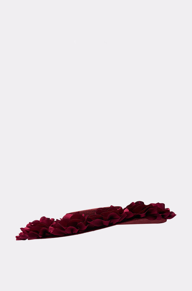 The ROSEY CLIP ON HAT, a flat, burgundy accessory with 3D rose detailing and dark red ruffles around the edge, is displayed on a light gray background. 4
