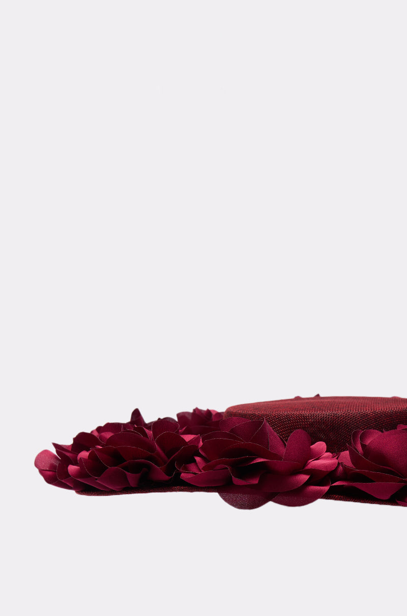 A close-up of the ROSEY CLIP ON HAT in maroon, featuring layered fabric flowers and 3D rose details along the brim, set against a plain light background. 6