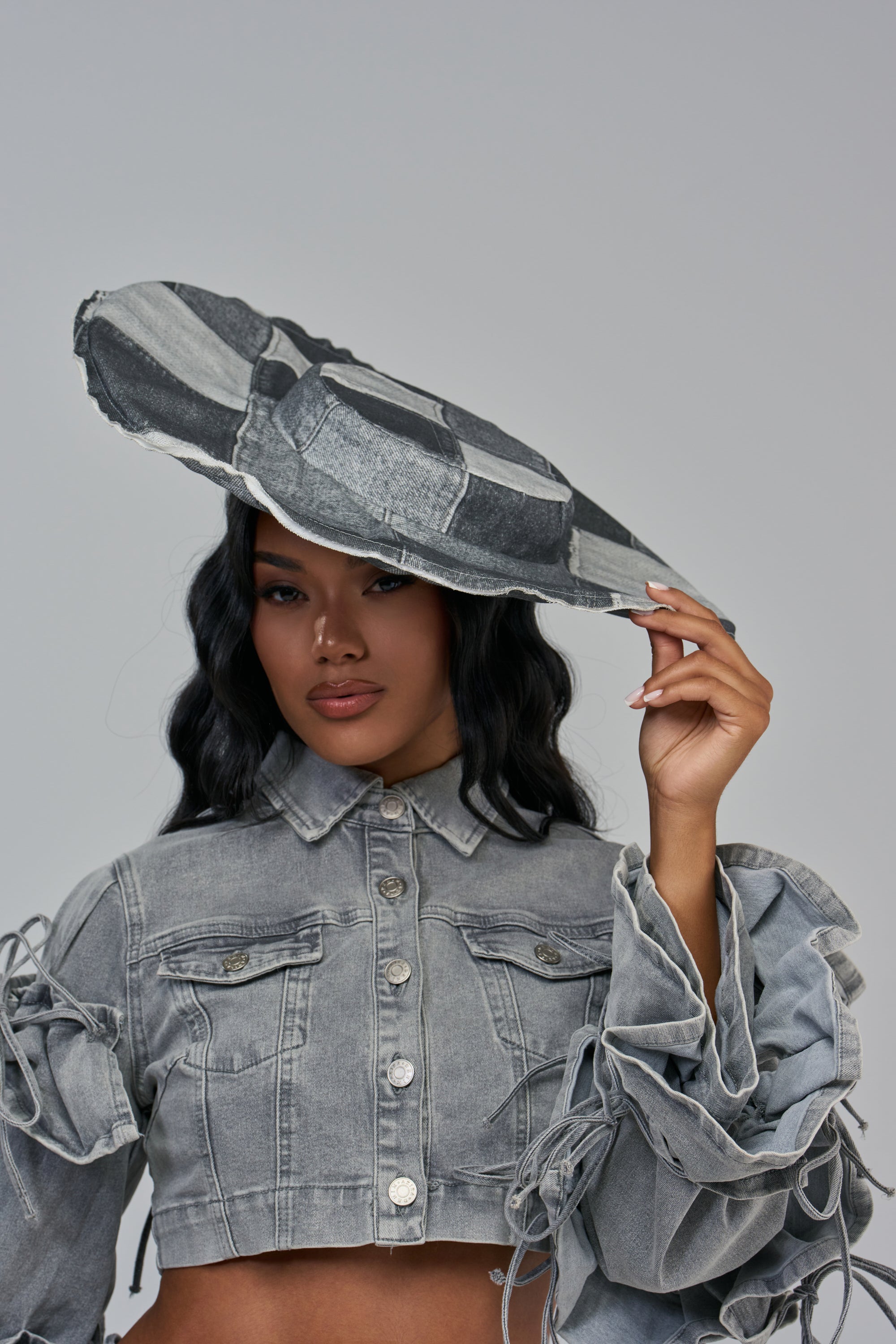 A person wearing a cropped denim jacket and a large-brimmed grey patchwork LOVER GIRL DENIM BRIM HAT.